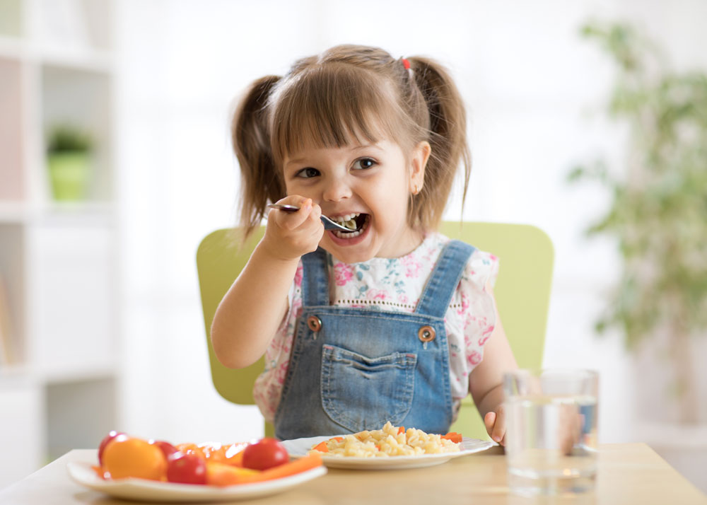 Kleines Mädchen isst Mittagessen mit Gemüse und trinkt Wasser